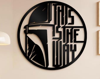 Może przedstawiać: Czarna metalowa grafika ścienna z okrągłym wzorem. Przedstawia sylwetkę hełmu i napis "THIS IS THE WAY". Grafika jest zamontowana na jasnej ścianie, tworząc uderzający kontrast. Projekt jest popularnym motywem.