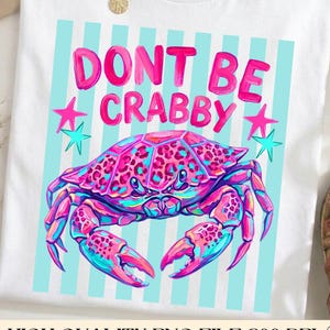 May include: White t-shirt with a colorful crab graphic and the text "DONT BE CRABBY". The crab is pink, blue, and purple, with a leopard print design. The shirt also features pink stars and blue stripes.