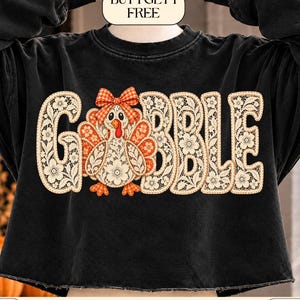 May include: A black long-sleeve sweatshirt featuring a graphic print of a turkey with a plaid bow and the word GOBBLE, where the letters and turkey are filled with a cream-colored floral lace pattern. The text BUY 1 GET 1 FREE is at the top.