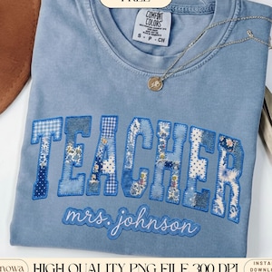 May include: A light blue Comfort Colors t-shirt with the word "TEACHER" in patchwork letters. The letters are various shades of blue with floral and gingham patterns. Below the word "TEACHER" is the name "mrs. johnson" in cursive. A silver necklace with a pendant is on the shirt.