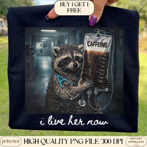 May include: Navy blue t-shirt featuring a raccoon wearing a stethoscope and holding a bag of coffee labeled "CAFFEINE". The text "i live her now" is below the graphic. The shirt also has the text "BUY 1 GET 1 FREE".