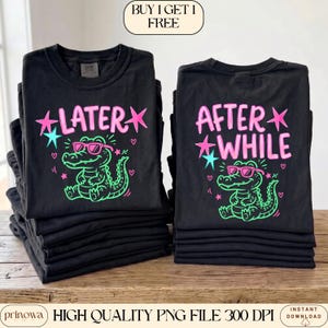 May include: Black t-shirts with neon green and pink graphics. One shirt says "LATER" with a cartoon alligator wearing sunglasses. The other says "AFTER WHILE" with a similar alligator design. The shirts are stacked on a wooden surface.