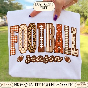 May include: A white t-shirt featuring the word FOOTBALL in large, block-style letters with varied patterns including orange gingham, tan polka dots, leopard print, brown stripes, and football graphics, with the word season in brown script below.
