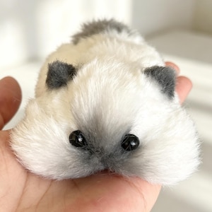 May include: A handmade plush toy in the shape of a small animal, featuring soft white fur with gray accents on the ears and back. The toy has black bead eyes and a gray nose, creating a cute and cuddly appearance.