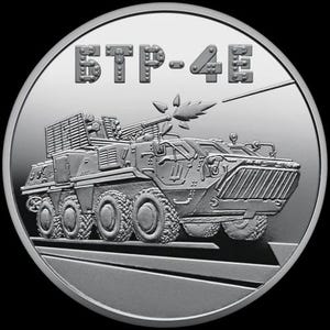 May include: A silver coin featuring a detailed depiction of a military vehicle, possibly an armored personnel carrier, with the text "БТР-4Е" at the top. The vehicle is shown in profile, with multiple wheels and a prominent weapon system. The coin has a reflective surface.