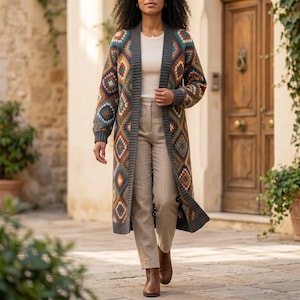 Könnte beinhalten: Eine lange, offene Strickjacke mit einem mehrfarbigen Rauten-Häkelmuster in Blau-, Orange- und Cremetönen, abgerundet durch einen dunkelgrauen Rippstricksaum. Sie wird über einem cremefarbenen Ripp-Oberteil und einer hellbeigen Hose mit braunen Stiefeln getragen.