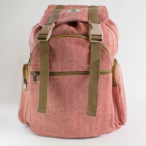 May include: A red and white herringbone patterned backpack with tan straps and buckles. The bag features a top flap, a front zipped pocket, and side pockets. The backpack is made from a sturdy fabric and is suitable for carrying books, travel items, or everyday essentials.