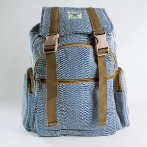 May include: Blue and white herringbone backpack with brown straps and accents. The backpack features a top flap with a buckle closure, two side pockets, and a front zip pocket. The bag has a tag that says "Just Hemp Made in Nepal".