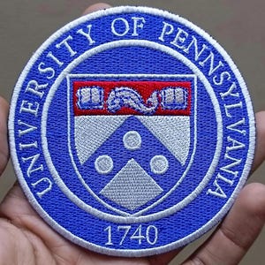 May include: Embroidered patch featuring the University of Pennsylvania's emblem. The patch is circular, with a blue border and white text that reads "UNIVERSITY OF PENNSYLVANIA." The center displays the university's crest in red, white, and blue, with the year "1740" at the bottom.