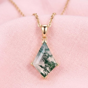 May include: A kite-shaped moss agate pendant featuring translucent stone with dark green dendritic inclusions, set in a gold-toned metal frame. The pendant hangs from a matching gold-toned chain, showcasing a faceted surface and a pointed bottom.