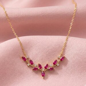 Peut inclure: Un collier à chaîne dorée avec un pendentif en forme de V composé de pierres rose foncé taille marquise et de petites pierres rondes transparentes. Le motif du pendentif évoque une branche délicate, centré sur une fine chaîne en métal doré.