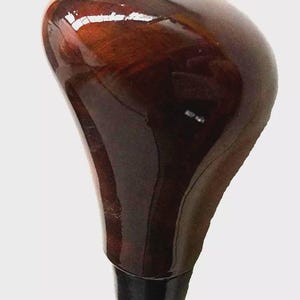 May include: A polished, dark brown wooden gear stick knob with a black base. The knob has a smooth, rounded top and a tapered shape, reflecting light. The wood grain is visible through the polished finish.
