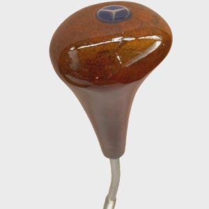 Puede incluir: Una cabeza de palo de golf marrón y bronce con un emblema azul en la parte superior. El palo tiene un acabado brillante y un eje transparente y curvado.