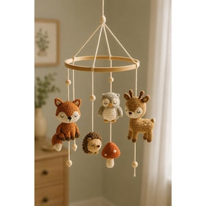 May include: A hanging nursery mobile featuring a circular wooden frame with five crocheted figures suspended by white strings. The figures include a rust-colored fox, a gray owl, a brown deer, a brown hedgehog, and a small red and white mushroom.