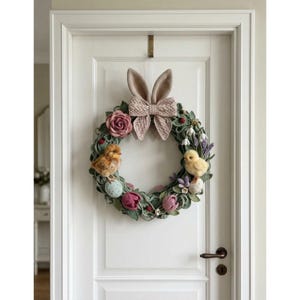 Puede incluir: Una corona de Pascua hecha a mano con un acento de orejas de conejo y lazo. La corona está decorada con rosas rosas, tulipanes y lavanda, junto con dos pollitos esponjosos y huevos decorativos. Colgada en una puerta blanca.