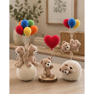 Peut inclure: Trois décorations en crochet avec des oursons. L'une présente deux ours sur une sphère crème tenant cinq ballons colorés. Une autre montre un ours sur un socle en bois tenant un ballon cœur rouge. La troisième montre un ours sortant d'une sphère.