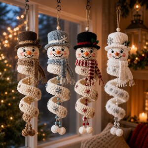 Könnte beinhalten: Vier gehäkelte Schneemann-Ornamente, die vertikal hängen. Jeder besteht aus einem Zylinder, einem Schal und einem langen, spiralförmigen Körper, der mit Schneeflocken-Applikationen verziert ist, in den Farben Braun, Hellblau, Schwarz und Weiß.