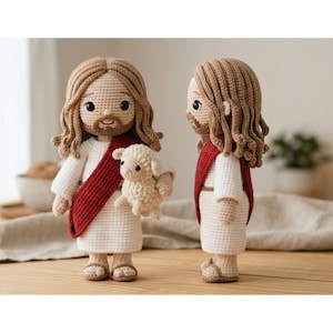 May include: Two handmade crochet dolls of a religious figure, one holding a small lamb. The dolls have light brown hair, beards, and are wearing white robes with a red sash. The lamb is beige. The dolls are standing on a wooden surface.