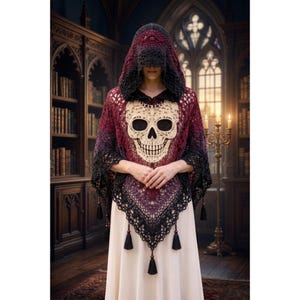 May include: A hooded crochet poncho featuring a gradient of black and deep red yarn. The centre displays a large, cream-coloured skull motif. The hem is finished with a black lace-like border and several small black tassels hanging from the bottom edge.