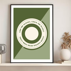 Puede incluir: Impresión artística enmarcada con un diseño geométrico en tonos verdes y crema. La impresión presenta un diseño circular con la cita "Chip the glasses, crack the plates! That's what Bilbo Baggins hates!" en una fuente serif.