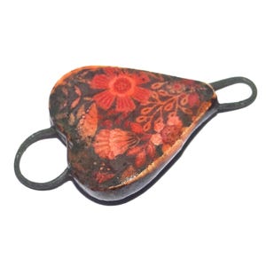 May include: Heart-shaped pendant with a floral design in shades of red, orange, and brown. The pendant has a dark metal frame with two loops. The floral pattern includes flowers and leaves.