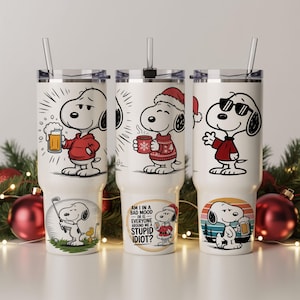 May include: Three white insulated tumblers with Snoopy illustrations. One shows Snoopy with a beer, another with a mug, and the third wearing sunglasses. Each tumbler has a straw and a different Snoopy graphic at the base. One has the text: "AM I IN A BAD MOOD OR IS EVERYONE AROUND ME A STUPID IDIOT?"