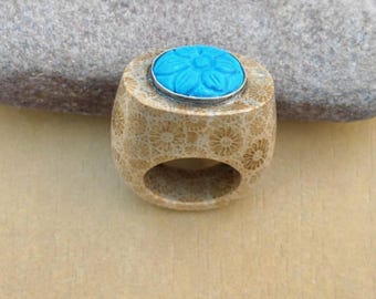 May include: A beige ring with a floral pattern and a turquoise flower-shaped stone set in a silver bezel. The ring is made of a porous material and has a rounded shape with a large opening for the finger.