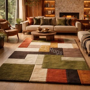 May include: A living room scene featuring a large, colorful area rug with a geometric pattern. The rug has blocks of brown, green, orange, and cream colors. A beige sofa with decorative pillows sits on the rug. The room has wooden accents and a fireplace.