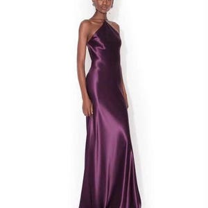 May include: A floor-length, deep purple satin gown featuring a high halter neckline with thin straps that wrap around the neck. The dress has a sleeveless design, a fitted bodice, and a long, flowing skirt that reaches the floor with a subtle sheen.