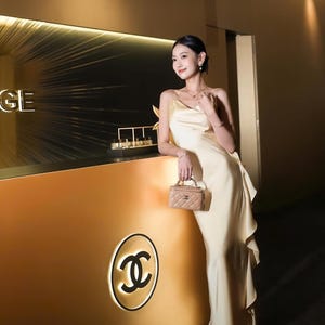 May include: A floor-length, pale yellow satin slip dress with thin spaghetti straps and a ruffled side detail, paired with a small, beige, quilted leather vanity bag featuring a gold-tone interlocking CC logo and a top handle.