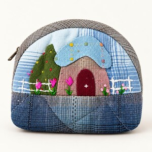 May include: A semi-circular fabric coin purse featuring a patchwork design of blue and grey textiles. The front displays an embroidered scene of a small house with a dark red door, a blue roof, a green tree, and a white fence with pink flowers.