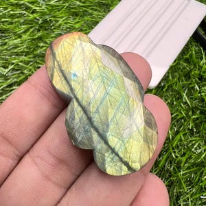 May include: A polished labradorite gemstone with a faceted surface, displaying iridescent flashes of yellow, gold, and blue. The stone has a rounded, multi-lobed shape with a smooth, reflective finish that highlights its natural mineral inclusions.