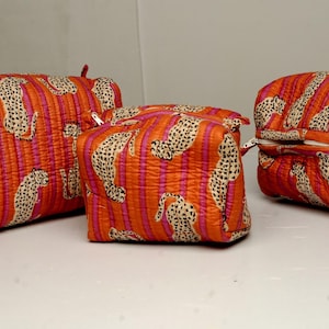 Puede incluir: Juego de tres neceseres naranjas con estampado de rayas verticales y estampado de leopardo. Las bolsas son de diferentes tamaños y tienen cierre de cremallera. Las bolsas están hechas de tela acolchada.