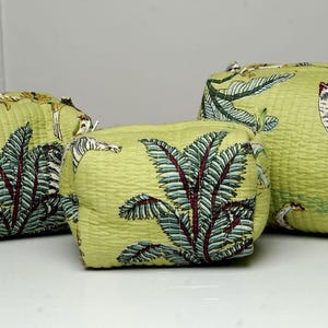 Puede incluir: Tres neceseres de tela verde con un estampado de aves tropicales y follaje. Las bolsas son de diferentes tamaños, con un aspecto texturizado. El diseño incluye tucanes, hojas y otros elementos tropicales.