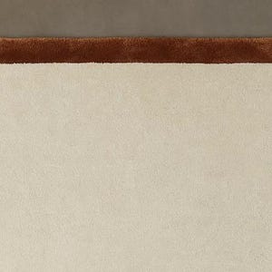 May include: A cream-colored rug with a brown border, shaped like a slice of bread. The rug has a soft, plush texture and a unique, playful design. This decorative rug is suitable for a bedroom or living room.
