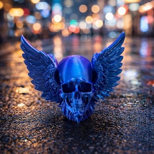 May include: A blue skull sculpture with feathered wings. The skull has detailed facial features and is set against a blurred background of city lights. The sculpture is made of a shiny material.