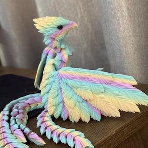 May include: A colorful, feathered bird sculpture in pastel shades of yellow, blue, pink, and purple. The bird has a detailed, textured design with a long, segmented tail and large wings. The sculpture is displayed on a wooden surface.