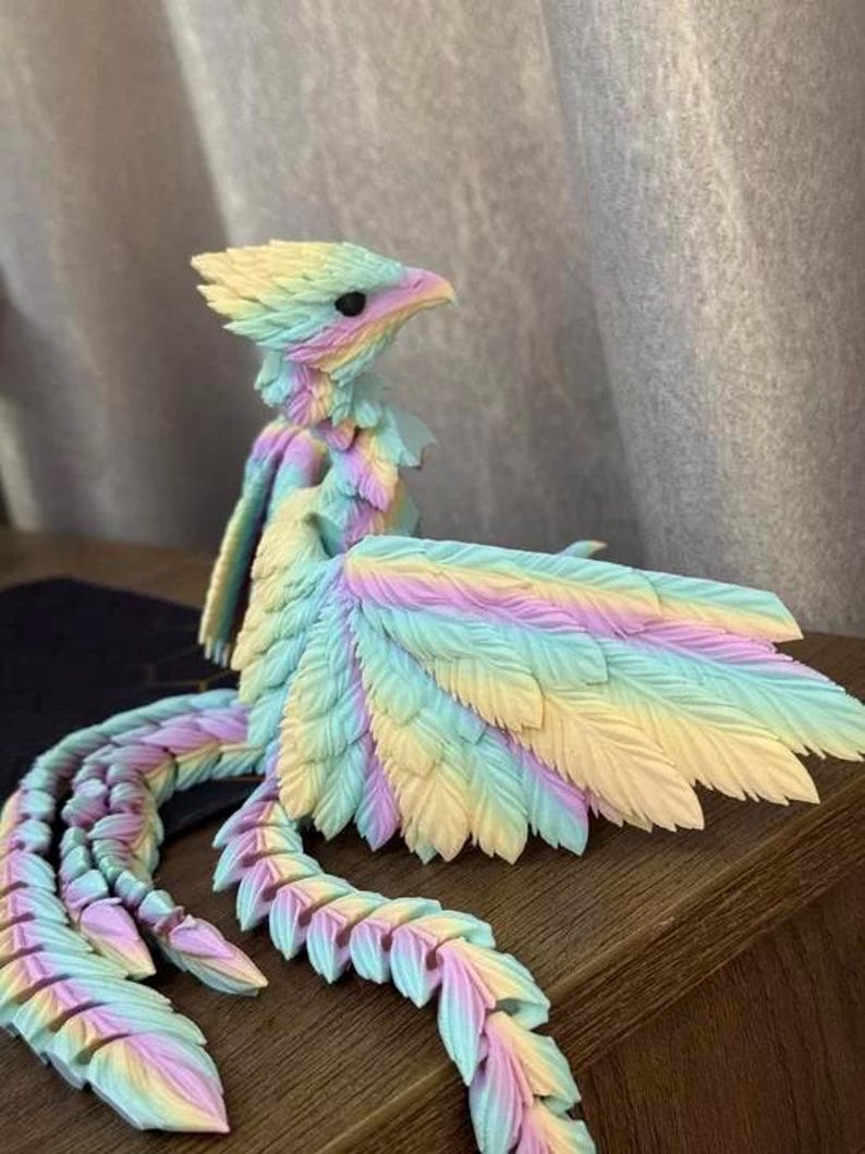 May include: A colorful, feathered bird sculpture in pastel shades of yellow, blue, pink, and purple. The bird has a detailed, textured design with a long, segmented tail and large wings. The sculpture is displayed on a wooden surface.
