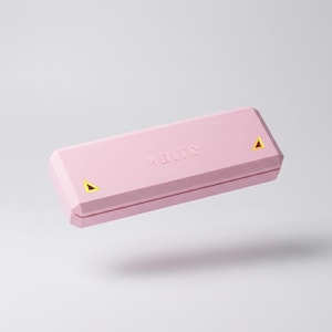 Puede incluir: Una caja rectangular rosa con la palabra "white" en relieve en la parte superior. La caja tiene un diseño geométrico con detalles de triángulos amarillos en cada extremo. La caja parece flotar sobre un fondo blanco.