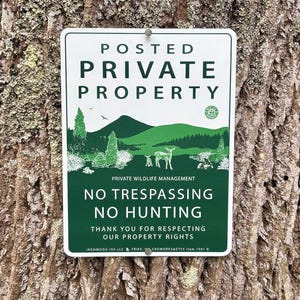 Pode incluir: Uma placa retangular branca e verde com as palavras "POSTED PRIVATE PROPERTY" no topo. Abaixo, uma ilustração de paisagem de um veado e árvores. A placa diz "NO TRESPASSING NO HUNTING".