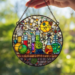 Puede incluir: Una vidriera redonda que representa una escena de laboratorio colorida con vasos de precipitados, matraces y otros equipos científicos. El diseño incluye tonos de amarillo, rojo, verde y azul, con una cadena negra para colgar. Aproximadamente 20 cm de diámetro.