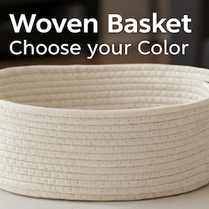 May include: A woven basket with a cream-colored exterior and two handles. The text "Woven Basket Choose your Color" is displayed at the top. The basket is round and appears to be made of a woven rope material.
