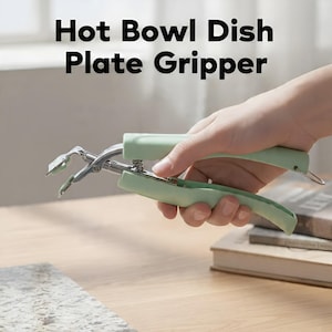 May include: A mint green hot bowl and plate gripper with stainless steel tongs. The text "Hot Bowl Dish Plate Gripper" is printed in black. The gripper is held in a person's hand.