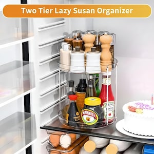 May include: A two-tier Lazy Susan organizer made of clear plastic and metal, filled with various kitchen items. The top tier holds spice jars and grinders, while the bottom tier contains bottles and jars. The text "Two Tier Lazy Susan Organizer" is at the top.