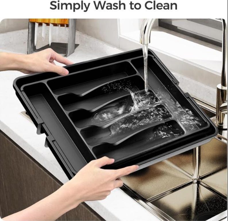 Puede incluir: Una bandeja de cubiertos de pl&aacute;stico negro con m&uacute;ltiples compartimentos se lava bajo un grifo. La bandeja es rectangular y est&aacute; dise&ntilde;ada para organizar la cuberter&iacute;a. El texto "Simply Wash to Clean" es visible en la parte superior de la imagen.
