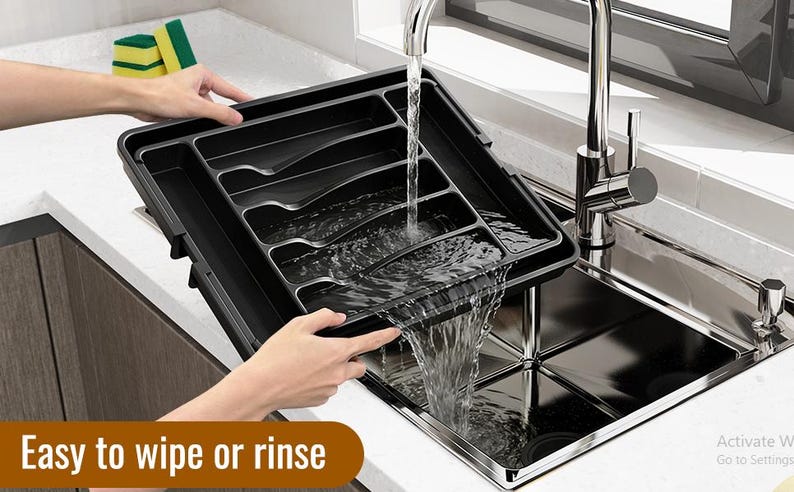 Puede incluir: Una bandeja negra para cubiertos con m&uacute;ltiples compartimentos se sostiene sobre un fregadero de acero inoxidable. El agua fluye de un grifo a la bandeja. El texto "Easy to wipe or rinse" se muestra en un cuadro marr&oacute;n en la parte inferior de la imagen.