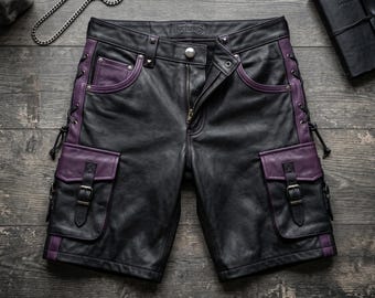 May include: Black leather shorts featuring purple side panels and pocket flaps. The shorts include side lacing, two large cargo pockets with buckle closures, silver-tone metal studs, a front zipper, and a button closure. The brand name Nocturnus is visible.