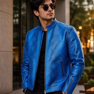 May include: A vibrant blue jacket featuring a textured snakeskin pattern, a stand-up collar, and a central silver zip. The garment includes two side pockets with silver zips and zipped cuffs, worn over a plain black shirt.
