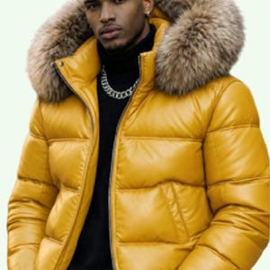 Puede incluir: Una chaqueta acolchada de color amarillo brillante con una capucha grande y gruesa con ribete de piel sintética en tonos marrón y bronceado. La chaqueta tiene cierre de cremallera frontal, costuras horizontales y mangas largas con puños negros.