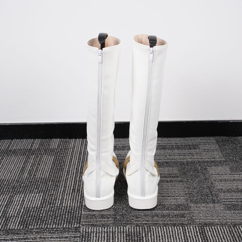 May include: A pair of white knee-high boots with a zipper down the back. The boots have a small heel and a tan accent near the ankle. The interior of the boot is a light tan color.